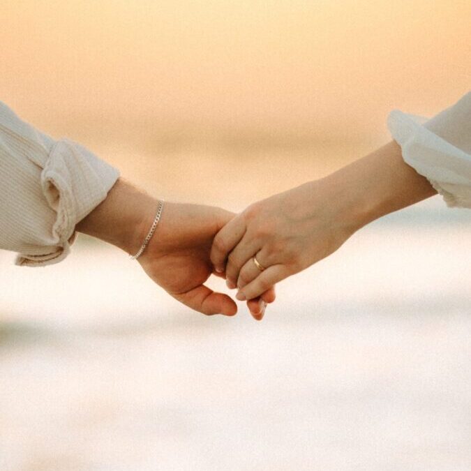 Close-up of couple's hands holding at sunset by the sea, symbolizing love and romance.