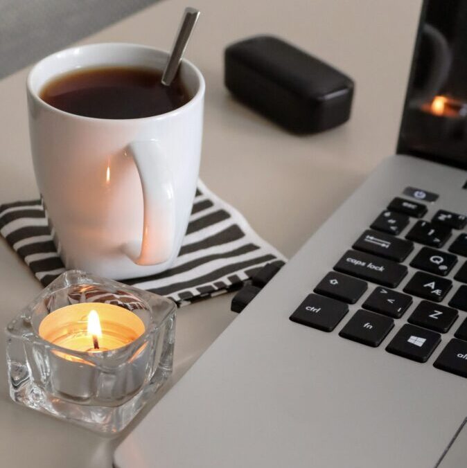 A relaxing workspace setup featuring a cup of tea, candle, and laptop for productivity.