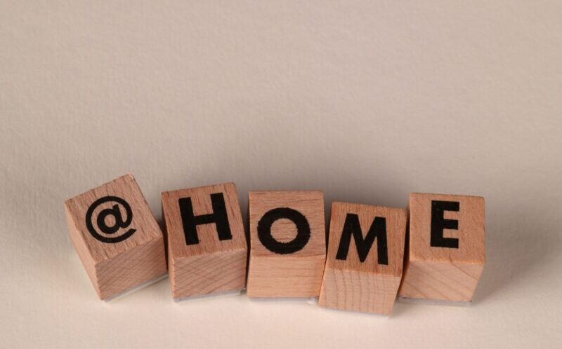 Wooden blocks spelling '@HOME' on a neutral beige background, symbolizing working or staying at home.