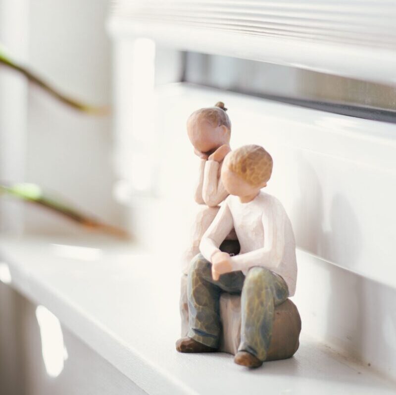 Two minimalist figurines sitting on a sunlit window ledge, conveying a sense of calm and affection.