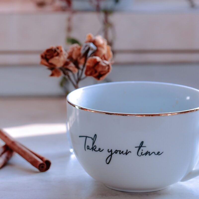 Porcelain cup with title and shiny surface against cinnamon sticks and dried rose bouquet on blurred background