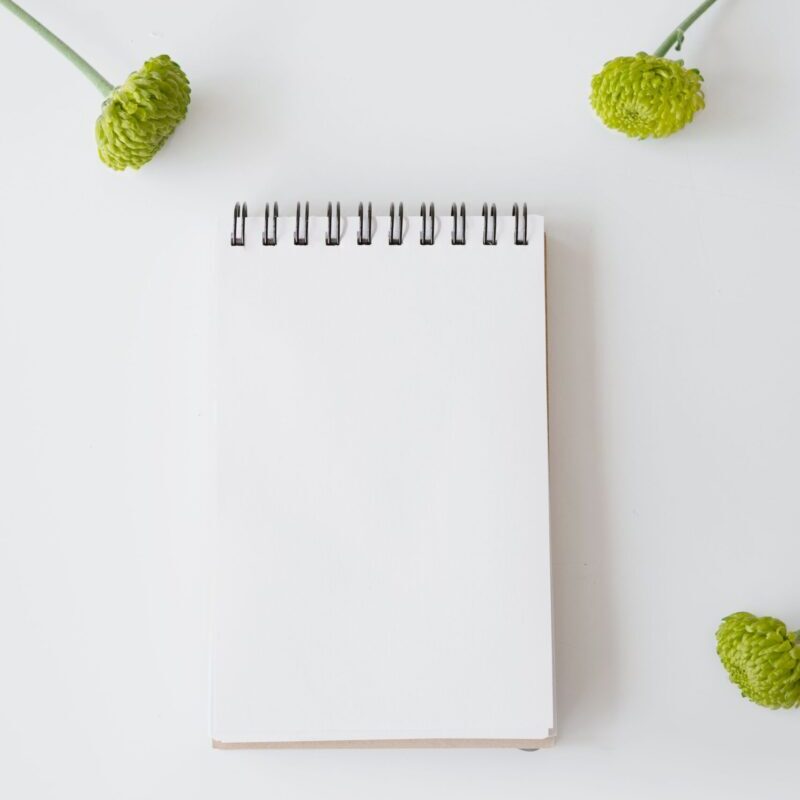Vertical notepad on white background with green flowers, perfect for copy space and design mockup.